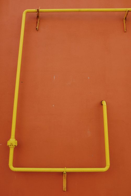 ellow gas pipes running along an orange exterior wall